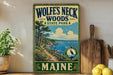 A vintage-style sign for Wolf's Neck Woods State Park in Maine, featuring a scenic illustration of a coastal landscape with pine trees, a winding path, and a body of water.