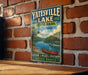 A vintage-style sign for Yatesville Lake, Kentucky, featuring a scenic illustration of a lake with a canoe, promoting outdoor activities and nature exploration.