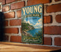 A vintage-style metal sign for Young State Park in Michigan, featuring a scenic landscape with a lake, mountains, and pine trees.