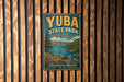 A vintage-style metal sign for Yuba State Park in Utah, featuring a scenic landscape with mountains, a lake, and a forest.