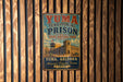A vintage-style metal sign for Yuma Territorial Prison, featuring a castle and a tower, is displayed on a wooden wall.