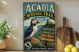 A vintage-style metal sign for the Acadia Birding Trail in Maine, featuring a puffin bird and various trail descriptions.