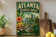 A vintage-style metal sign for the Atlanta Botanical Garden in Georgia, featuring a lush garden scene with flowers, plants, and a city skyline in the background.