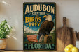a vintage-style sign for Audubon Center for Birds of Prey in Florida, with an eagle perched on a tree stump in the center.