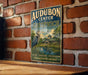A vintage metal sign for Audubon Center in Greenwich, Connecticut, featuring a bird and a building in the background.