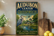 A vintage-style sign for Audubon Center in Greenwich, Connecticut, featuring an illustration of a heron and a pond surrounded by trees.