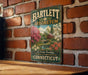 A vintage-style metal sign for the Bartlett Arboretum in Connecticut, featuring a scenic landscape with trees, flowers, and a bridge.