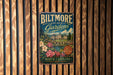 A vintage metal sign for Biltmore Estate Gardens in North Carolina, featuring a castle and garden scene.