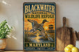 A vintage-style metal sign for the Blackwater National Wildlife Refuge in Maryland, featuring an illustration of a duck flying over a marshy area with a sunset in the background.
