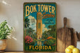 A vintage-style sign for the Bok Tower Gardens in Florida, featuring a tropical landscape with a tall tower and lush greenery.