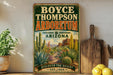 A vintage-style metal sign for the Boyce Thompson Arboretum in Arizona, featuring a desert landscape with cacti and other desert plants.