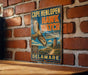 A vintage metal sign for Cape Henlopen Hawk Watch hangs on a brick wall, featuring an illustration of a hawk in flight and text promoting the conservation and education efforts of the area.