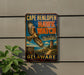 A vintage metal sign for Cape Henlopen Hawk Watch, featuring an illustration of a hawk in flight and a lighthouse in the background, mounted on a wall.