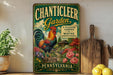 A vintage-style metal sign for "Chanticleer Garden" in Pennsylvania, featuring a rooster and colorful flowers, is displayed on a shelf next to a wooden cutting board and some potted plants.