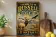 A vintage-style metal sign for Charles M. Russell National Wildlife Refuge in Montana, featuring an elk and a bald eagle in a mountainous landscape.