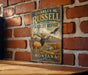 A vintage metal sign for Charles M. Russell's National Wildlife Refuge in Montana, featuring an elk and a bird in a scenic landscape.