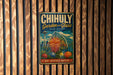 A vintage metal sign with the text "CHIHULY Garden & Glass WASHINGTON" and an illustration of a greenhouse, hanging on a wooden wall.