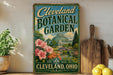 A vintage-style metal sign for the Cleveland Botanical Garden, featuring a colorful illustration of the greenhouse and surrounding landscape.