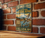 A vintage metal sign for Creamer's Field, a migratory waterfowl refuge in Alaska, featuring a duck flying over a lake with mountains in the background.