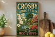 A vintage-style metal sign for the Crosby Arboretum in Mississippi, featuring a scenic landscape with trees, flowers, and a pond.