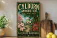 A vintage-style sign for the Baltimore Arboretum, featuring a painting of a house surrounded by flowers and a path leading to it.