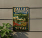 A vintage-style metal sign for the Dallas Arboretum and Botanical Garden, featuring a scenic landscape with a pond, trees, and flowers.