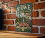A vintage-style metal sign for Daniel Stowe Botanical Garden in North Carolina, featuring a garden scene with a pond, flowers, and a fountain.