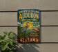 A vintage metal sign for Dauphin Island Audubon Bird Sanctuary in Alabama, featuring illustrations of birds and a lighthouse.