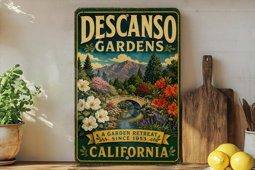 A vintage-style sign for Descanos Gardens, featuring a scenic landscape with a bridge, flowers, and mountains, is displayed on a shelf next to a potted plant and a cutting board.