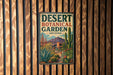 A vintage-style metal sign for the Desert Botanical Garden in Arizona, featuring a desert landscape with cacti, succulents, and a mountain backdrop.