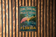 A vintage-style metal sign for Ding Darling National Wildlife Refuge in Sanibel Island, Florida, featuring a pink flamingo and a sunset landscape.