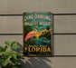 A vintage-style metal sign for the Ding Darling National Wildlife Refuge in Sanibel Island, Florida, featuring a pink egret and a dolphin in a tropical landscape.