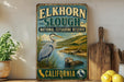 A vintage-style metal sign for Elkhorn Slough National Estuarine Reserve in California, featuring an illustration of a heron and an otter in a body of water.