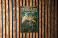 A vintage Everglades National Park sign is displayed on a wooden wall, featuring illustrations of birds and a sunset landscape.