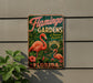 A vintage-style sign for Flamingo Gardens, featuring a pink flamingo and tropical foliage, is displayed on a wall.