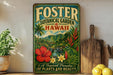 A vintage-style metal sign for Foster Botanical Garden in Hawaii, featuring a tropical landscape with palm trees, flowers, and a waterfall.