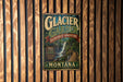A vintage metal sign for Glacier Garden, a rainforest adventure in Montana, hanging on a wooden wall.