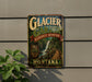 A vintage-style metal sign for Glacier Garden, a rainforest adventure in Montana, featuring a waterfall and a wooden walkway.