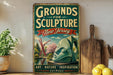 A vintage-style sign for "Grounds for Sculpture New Jersey" is displayed on a wooden shelf, with a potted plant and a wooden cutting board nearby.