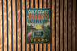 A vintage-style metal sign for the Gulf Coast Bird Observatory in Texas, featuring illustrations of birds and a tropical landscape.