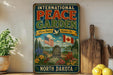 A vintage-style sign for the International Peace Garden in North Dakota, featuring an illustration of the garden with American and Canadian flags, surrounded by flowers and a peaceful landscape.