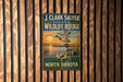 A vintage metal sign for the J. Clark Salyer National Wildlife Refuge in North Dakota, featuring a duck and a sunset landscape.