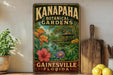 A vintage-style metal sign for the Kanapaha Botanical Gardens in Gainesville, Florida, featuring a tropical garden scene with a gazebo and various flowers.