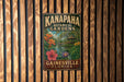 A vintage-style metal sign for Kanapaha Botanical Gardens in Gainesville, Florida, featuring a tropical garden scene with colorful flowers and a gazebo.