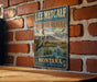 A vintage metal sign for the Lee Metcalf National Wildlife Refuge in Montana, featuring an illustration of a heron and a duck in a lake surrounded by mountains.
