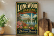 A vintage-style metal sign for Longwood Gardens in Pennsylvania, featuring a garden scene with a fountain and flowers, is displayed on a shelf next to a wooden cutting board and some potted plants.