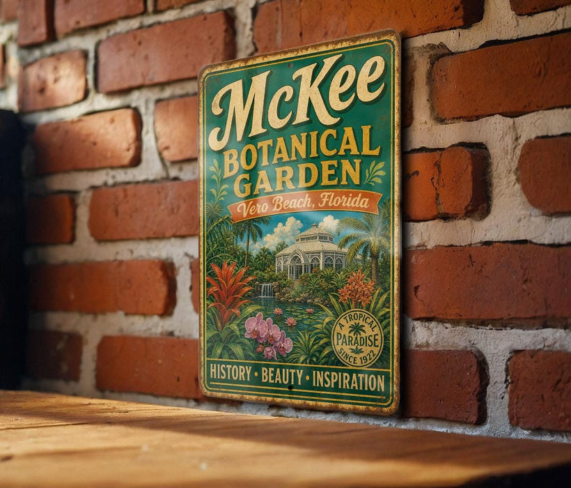A vintage-style metal sign for McKee Botanical Garden in Vero Beach, Florida, featuring a tropical garden scene with palm trees, flowers, and a gazebo.