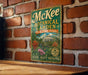 A vintage-style metal sign for McKee Botanical Garden in Vero Beach, Florida, featuring a tropical garden scene with palm trees, flowers, and a gazebo.