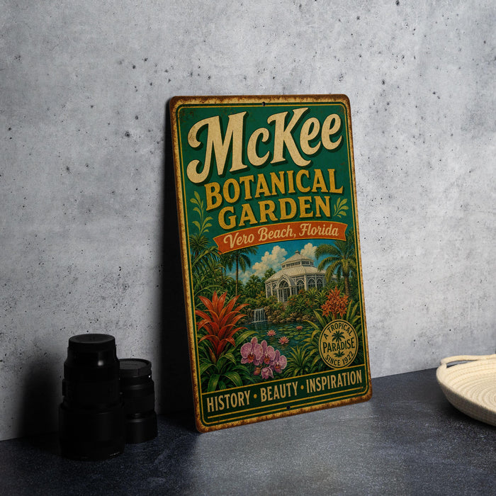 A vintage-style metal sign for McKee Botanical Garden in Vero Beach, Florida, featuring a tropical garden scene with palm trees, flowers, and a building.