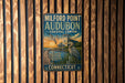 A vintage metal sign for Milford Point Audubon Coastal Center in Connecticut, featuring a seagull and a lighthouse, is displayed on a wooden wall.